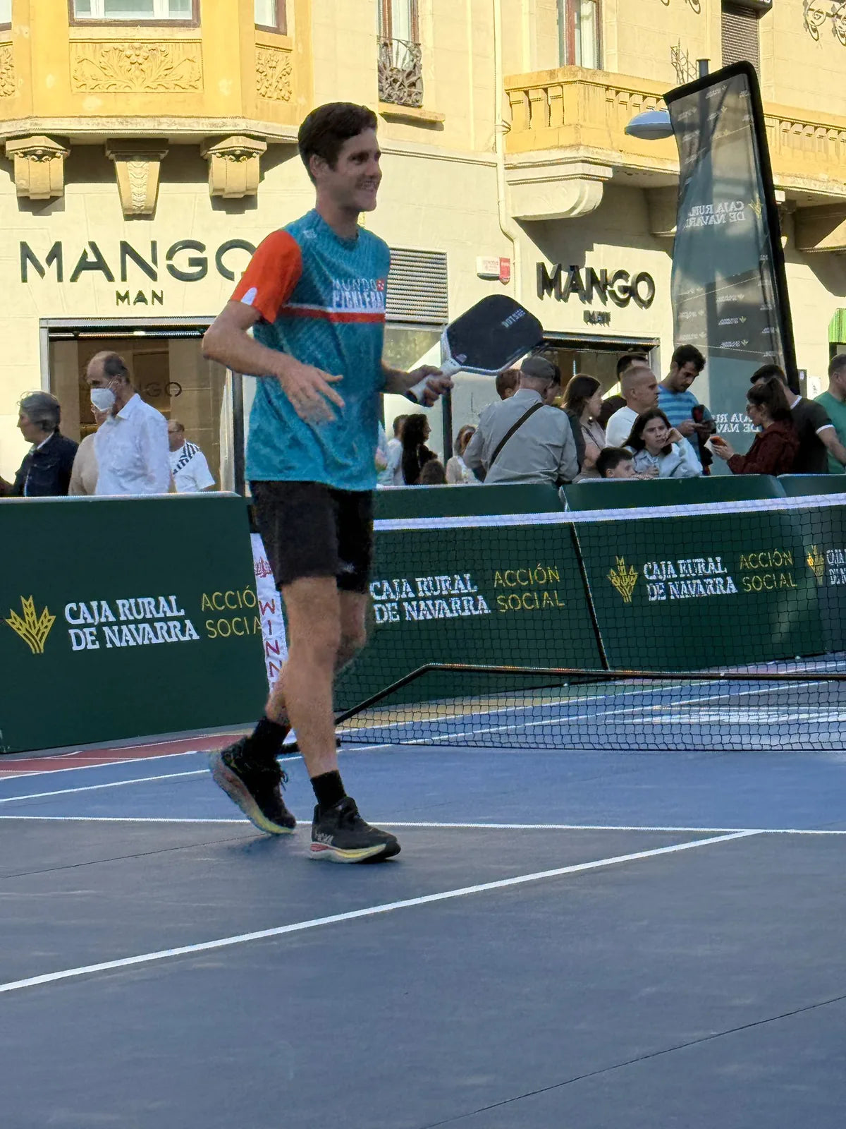 Jugador profesional caminando por la pista junto al perimetral publicitario del evento de pickleball