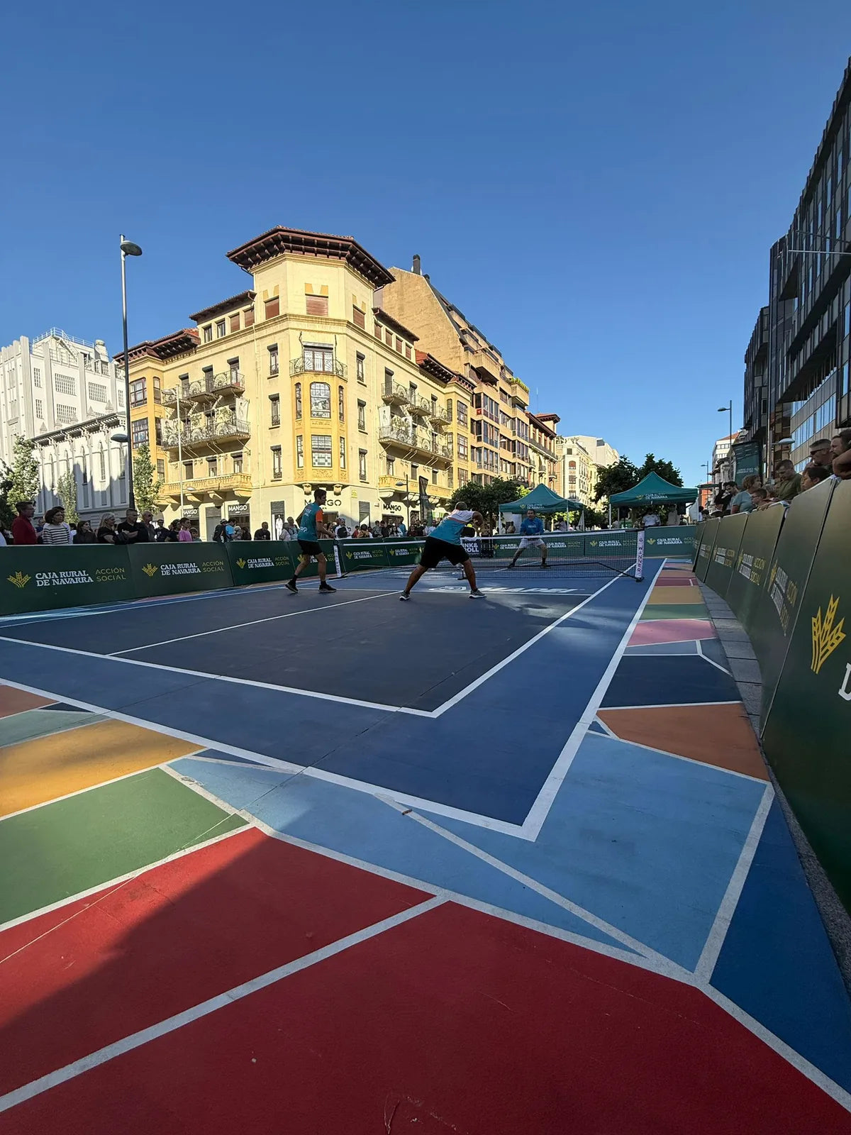 Vista completa de la pista de pickleball portatil montada en plaza publica con perimetral publicitario y edificios de fondo